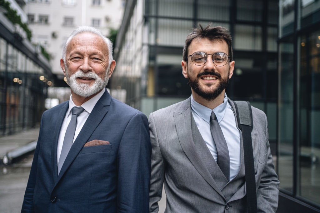 Cheerful business colleagues, a father and a son, standing in formalwear in front of an office building.